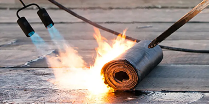 Torch applying heat to a roll of modified bitumen membrane on a flat roof deck