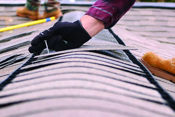 Roofer hand-nailing a replacement composition shingle during a targeted roof repair